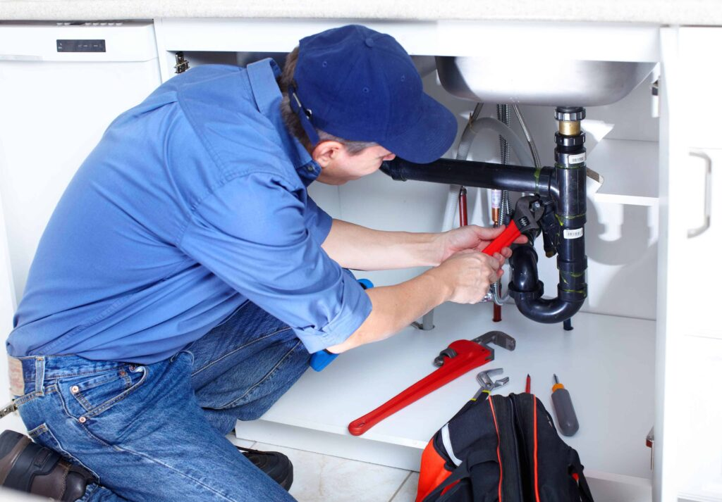 Professional plumber repairing pipes under kitchen sink